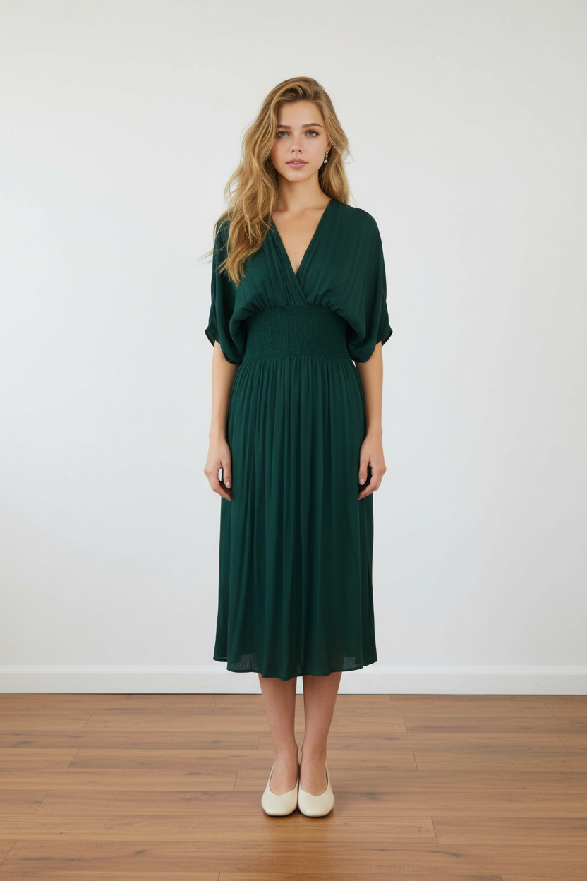 Woman wearing a green dress standing on a wooden floor with a white wall background